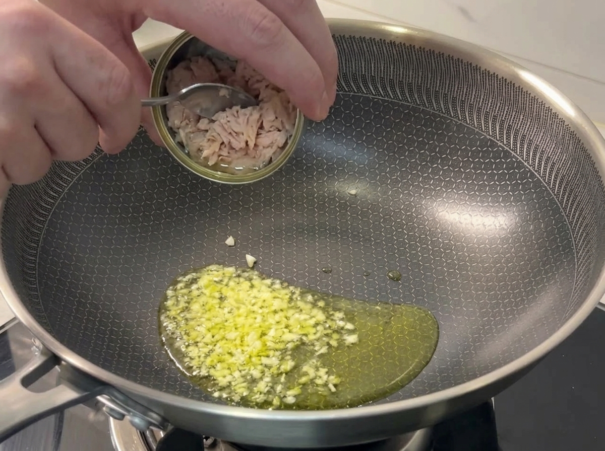 炒めたにんにくのフライパンにツナを入れる様子。