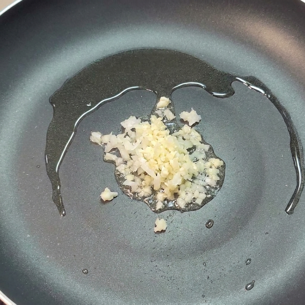 フライパンでオリーブオイルと一緒に炒められているみじん切りの玉ねぎとにんにく。