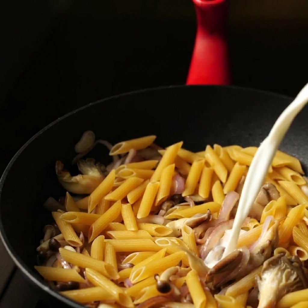 パスタと具材の上に牛乳と水の混合液を注いでいる様子。