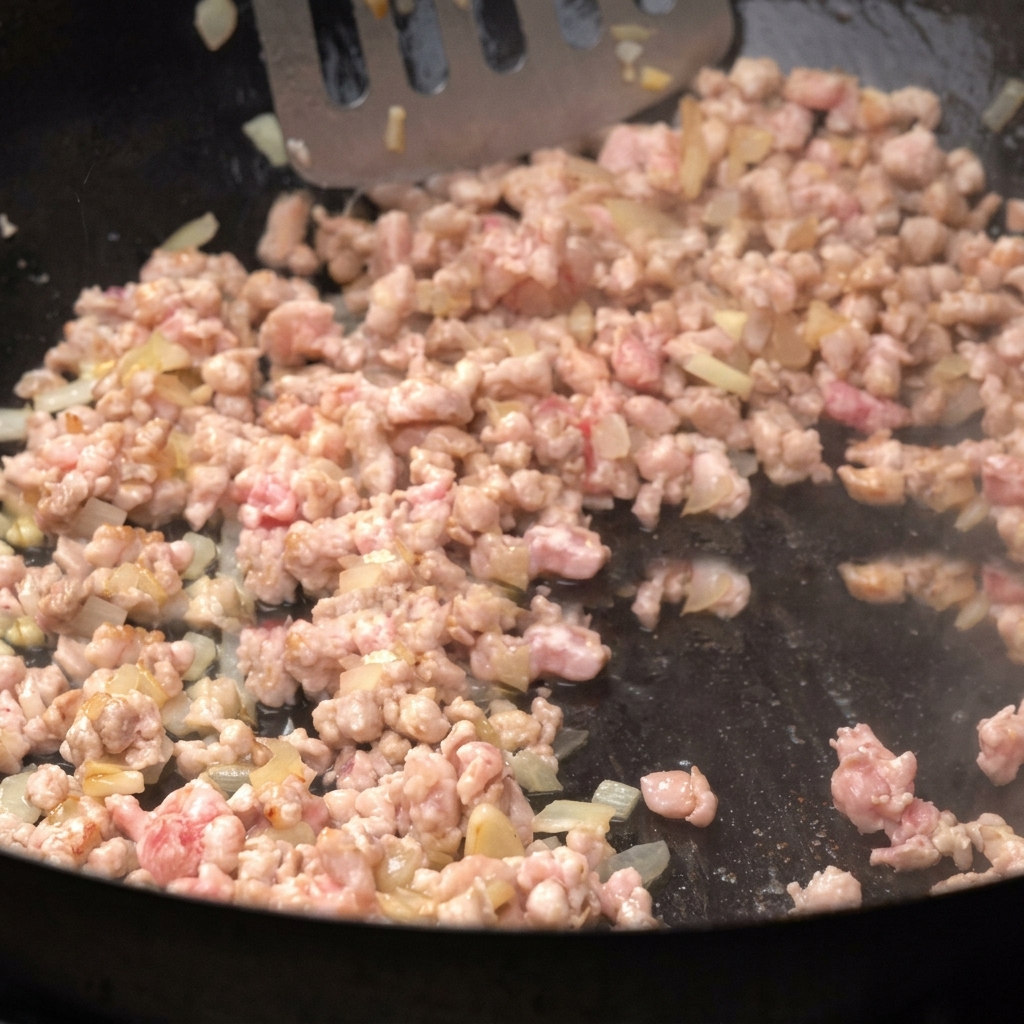 ひき肉を玉ねぎと一緒にフライパンで炒め、へらでほぐしている様子。