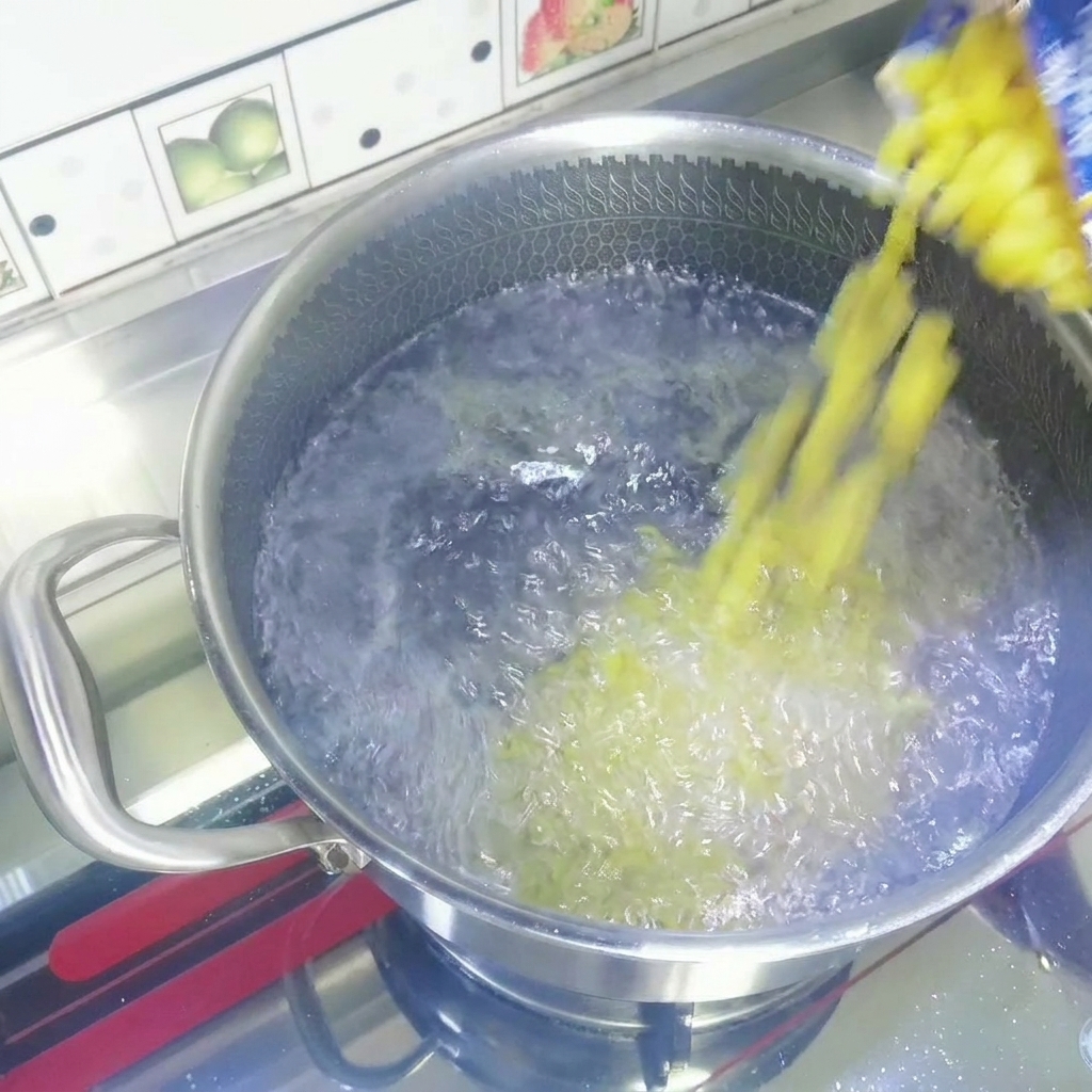 袋から沸騰したお湯の入ったステンレス製の鍋に、乾燥した黄色のマカロニを注いでいる様子。