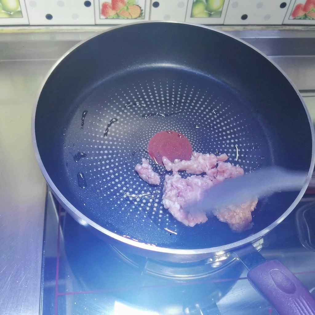 熱したフッ素樹脂加工のフライパンで、グレーのシリコンスパチュラを使って生のひき肉を炒めている様子。