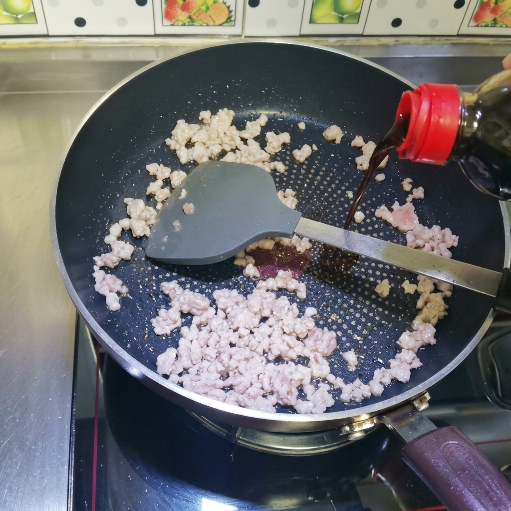熱したフライパンの中の炒めたひき肉に、ボトルから醤油を注いでいる様子。