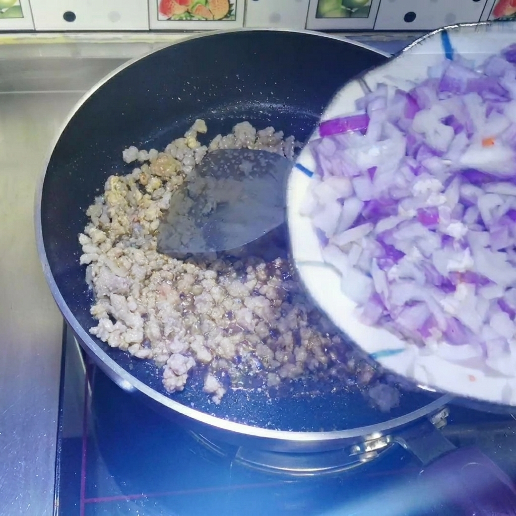 白いお皿から、ひき肉が入ったフライパンに角切りの赤玉ねぎを移している様子。