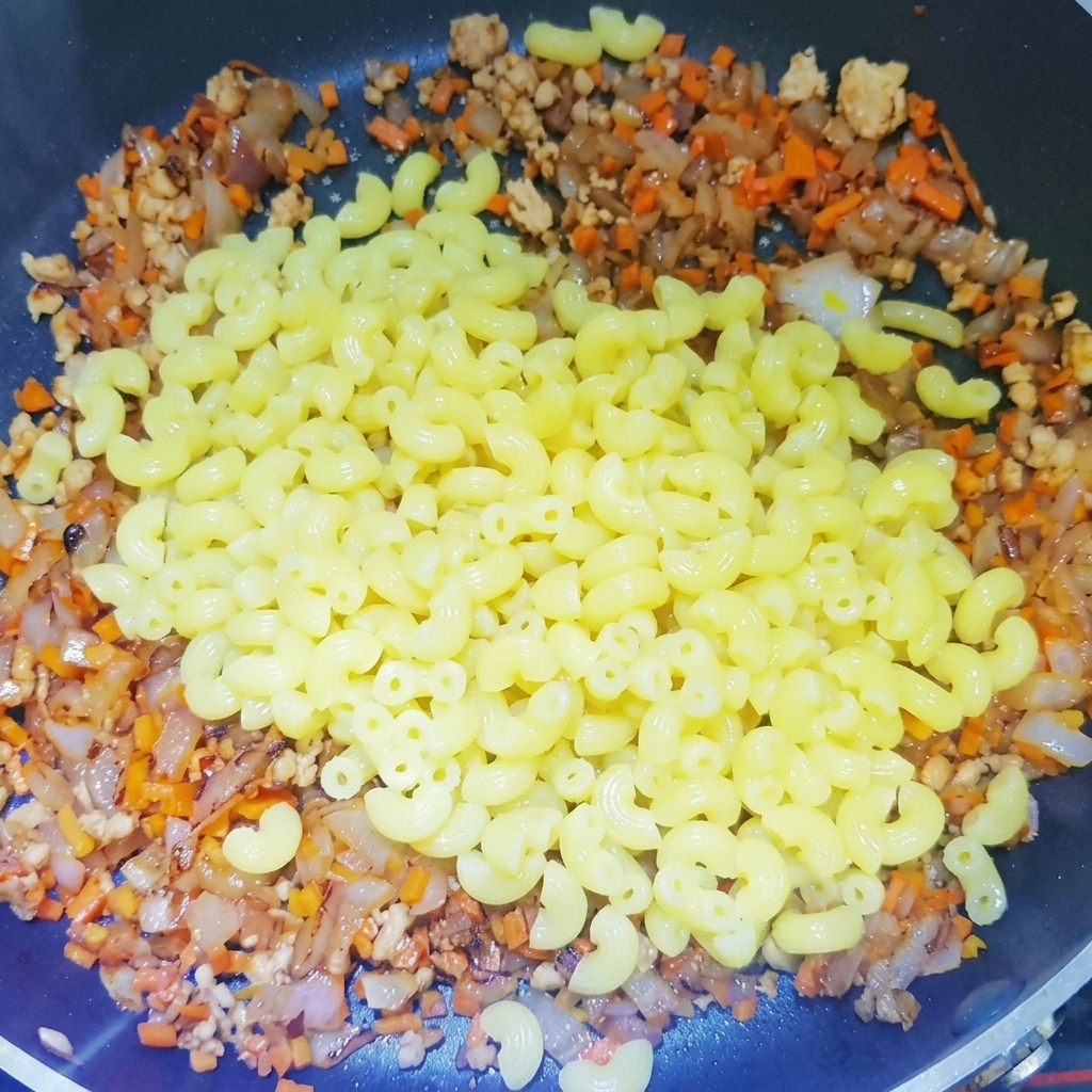 ひき肉、玉ねぎ、にんじんを炒めたベースが入ったフライパンに、茹でたマカロニを加えている様子。