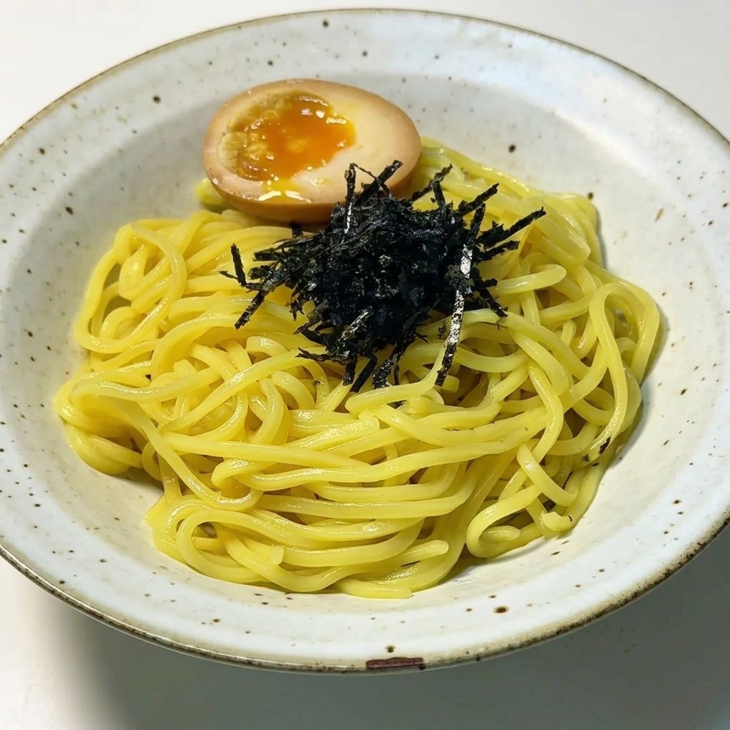 盛り付けた麺の上に、刻み海苔ととろりとした黄身の半熟卵が添えられている様子。