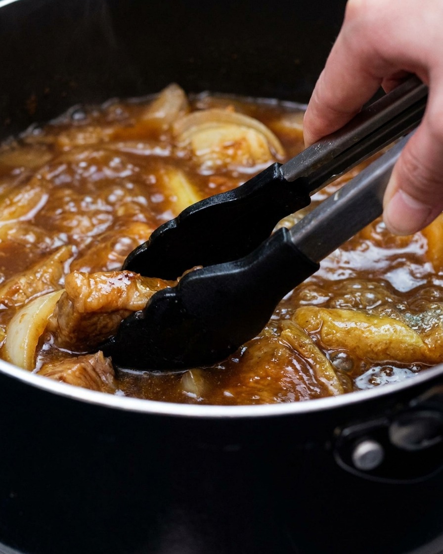 油揚げと長ねぎが入ったカレーつゆをトングで混ぜている様子。