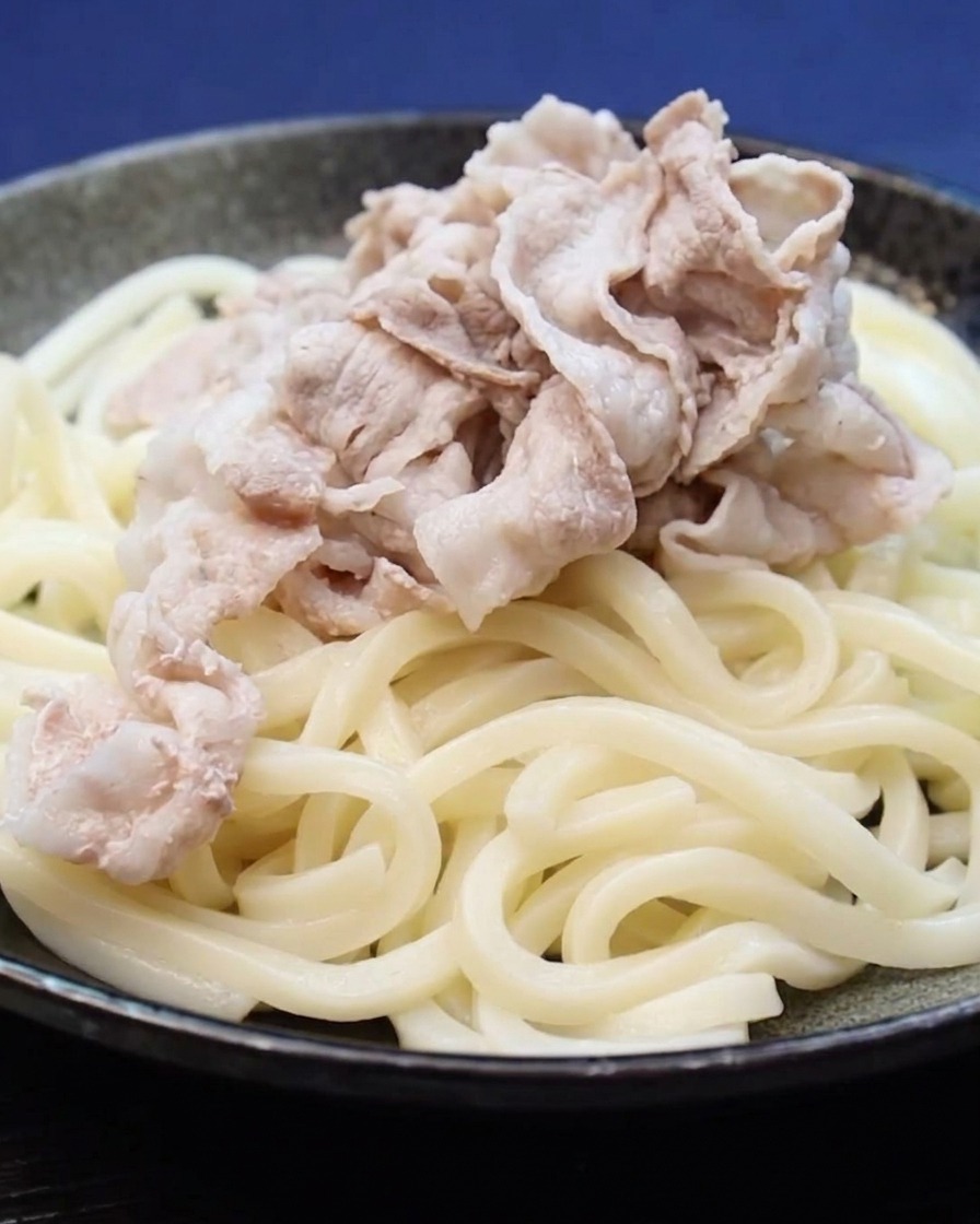 うどんの上に茹でた豚肉を盛り付けている様子。