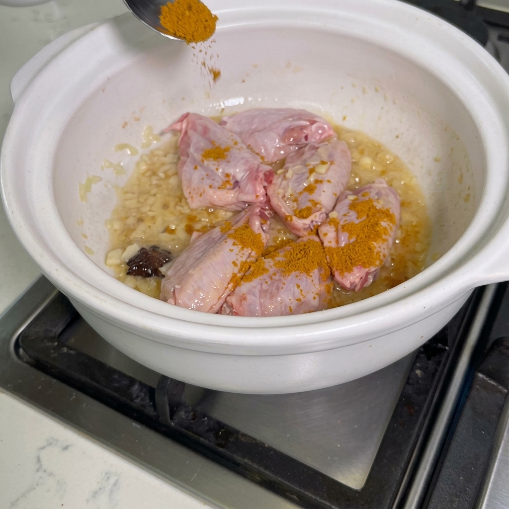 鍋の中の鶏手羽先にカレー粉を振りかけている様子。
