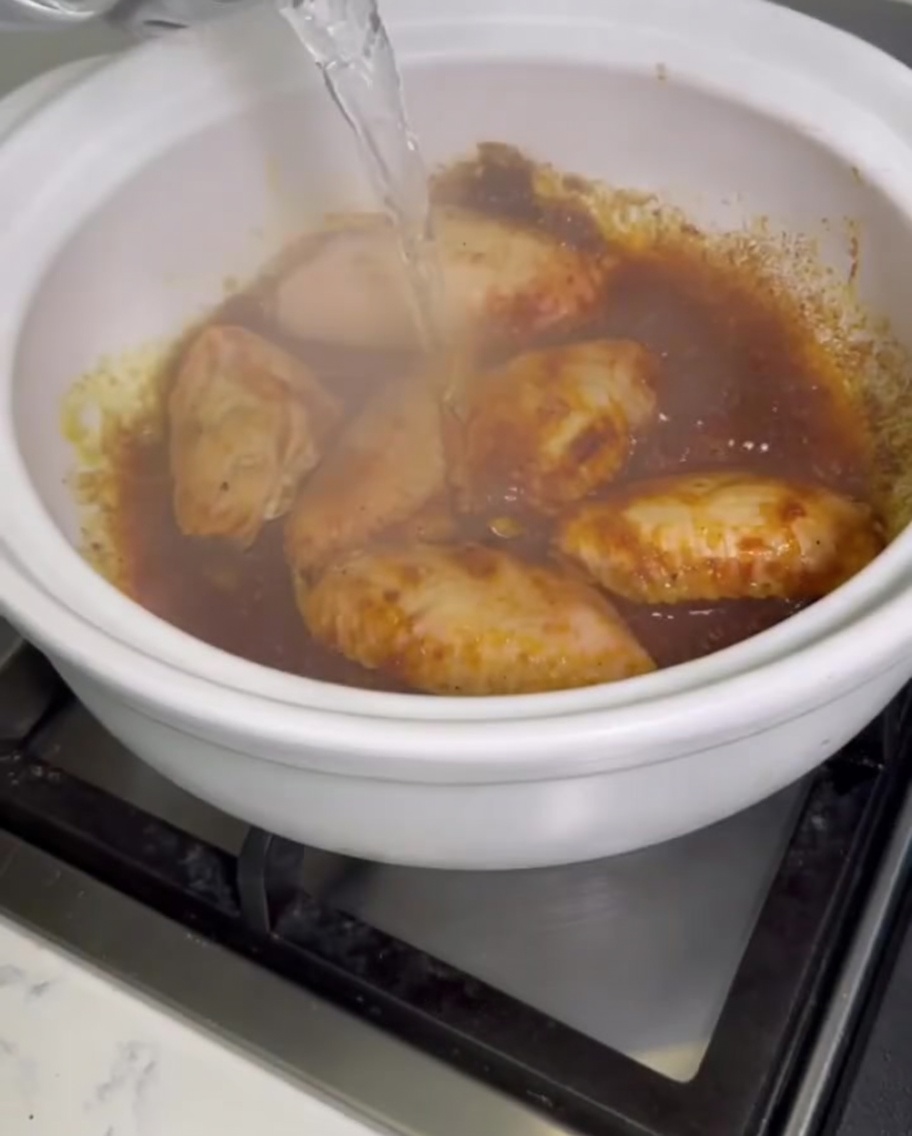 カレーの鶏手羽先が沸騰している土鍋に、容器から水が注がれている様子。