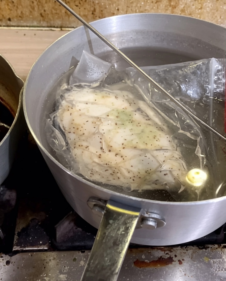 熱いお湯の入った鍋に沈められた、真空パック入りの鶏胸肉。