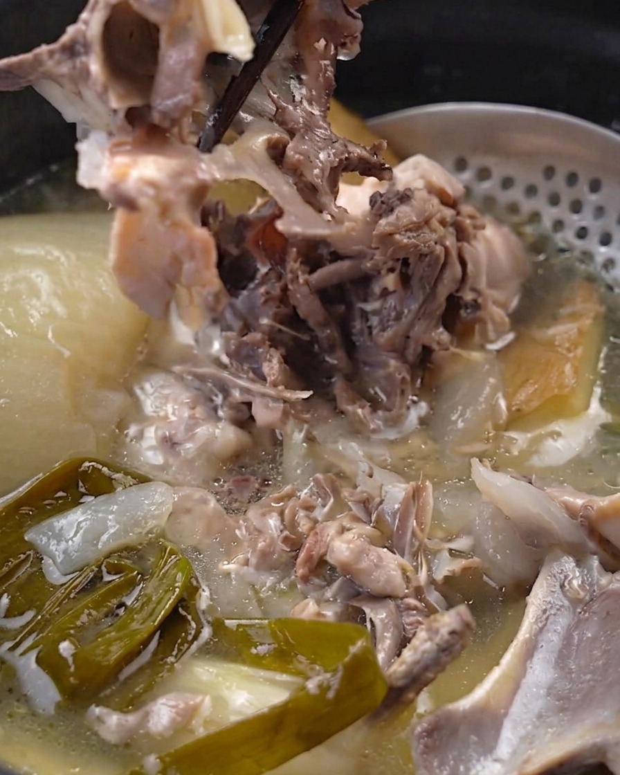 菜箸で圧力鍋の中の柔らかくなった鶏肉を骨から外している様子