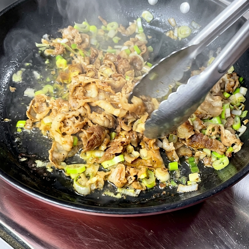 トングで牛肉を炒めながら水分を飛ばしている様子。