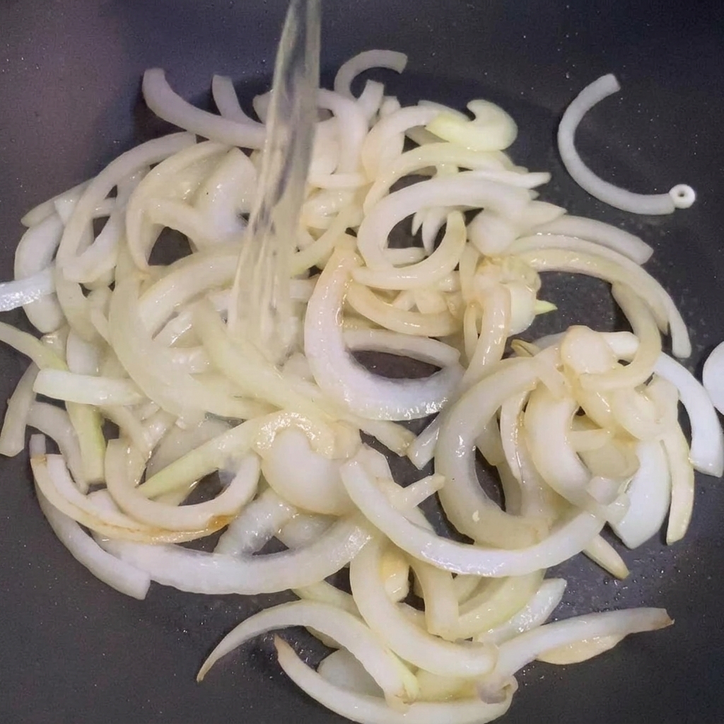 炒めた玉ねぎが入ったフライパンに酒を注ぐ様子。