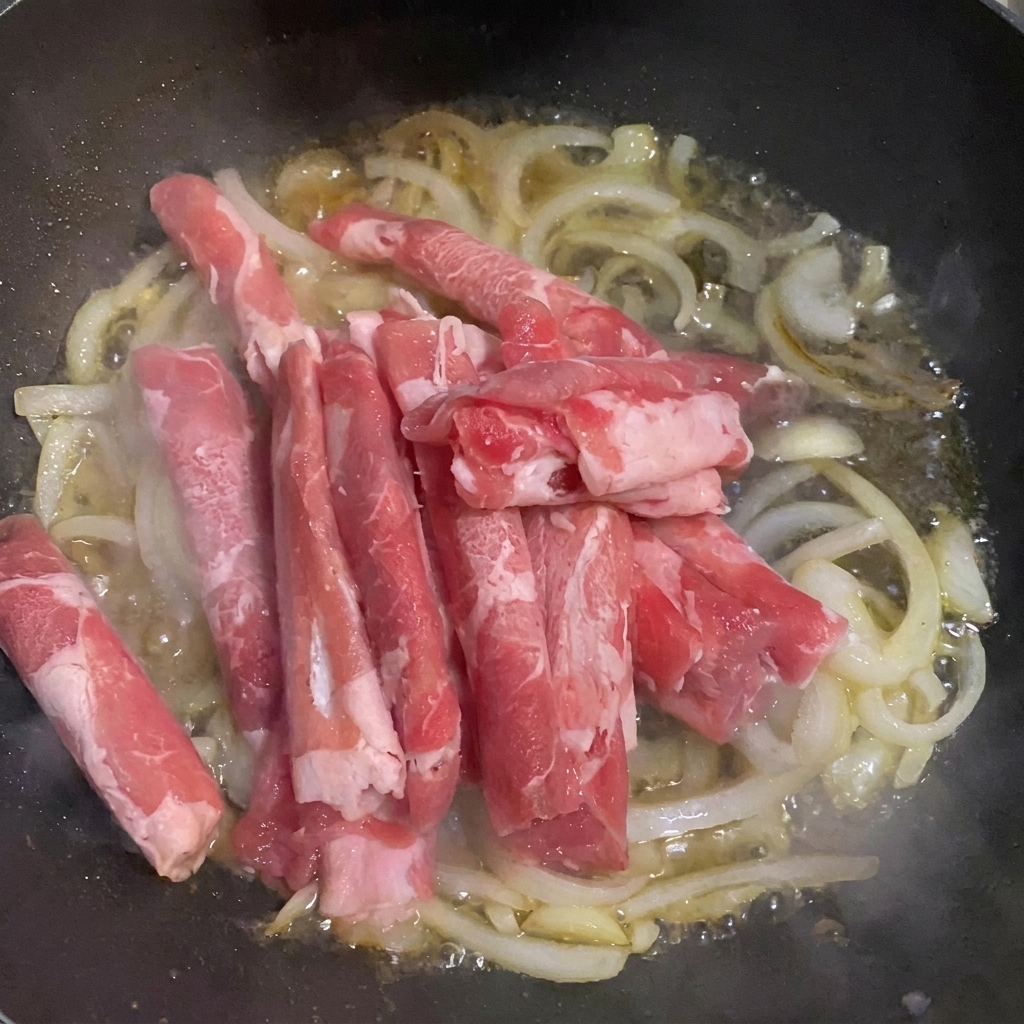玉ねぎと水が入ったフライパンに牛肉の薄切り肉を加える様子。