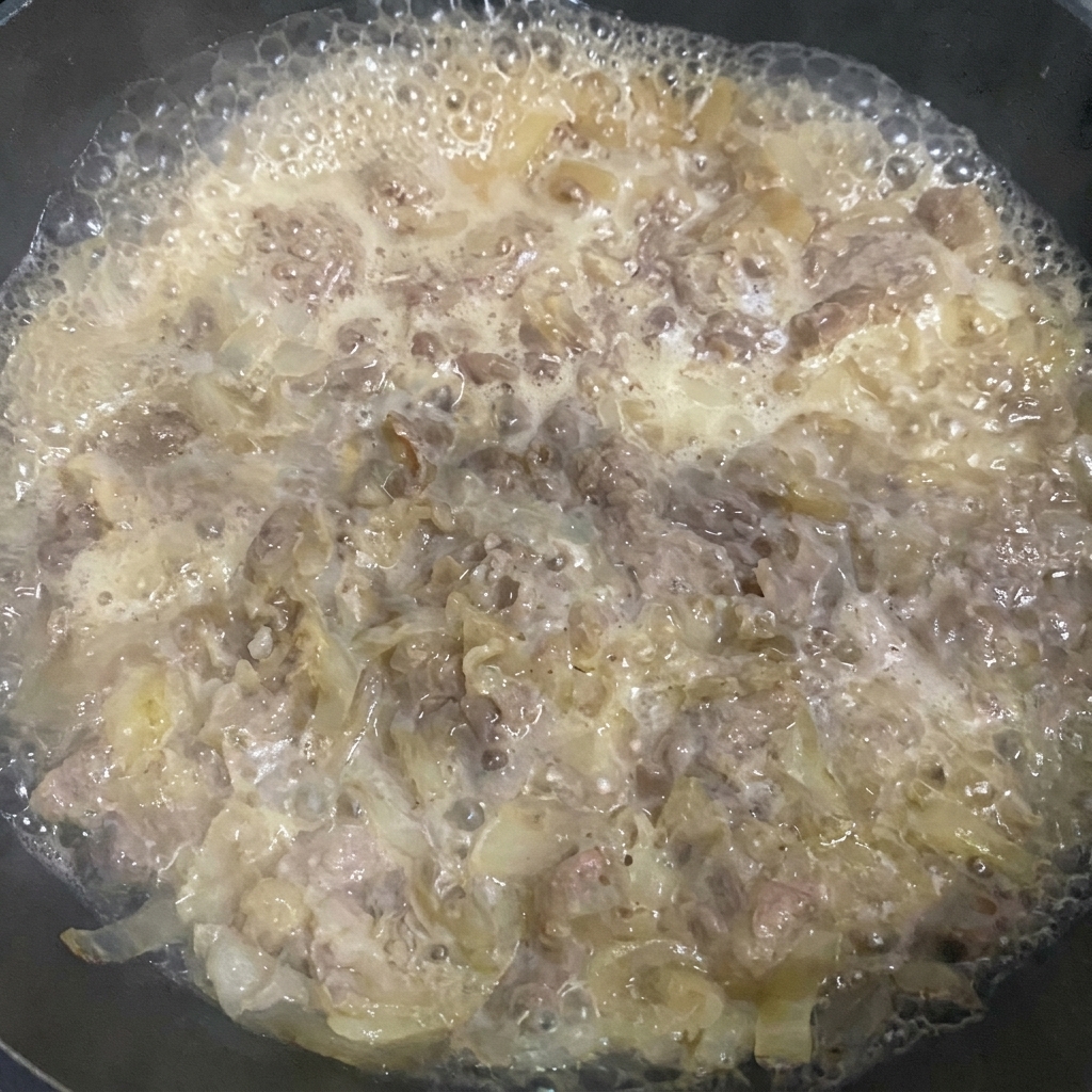 ヘラを使って煮込んでいる牛肉のアクを丁寧に取り除いている様子。