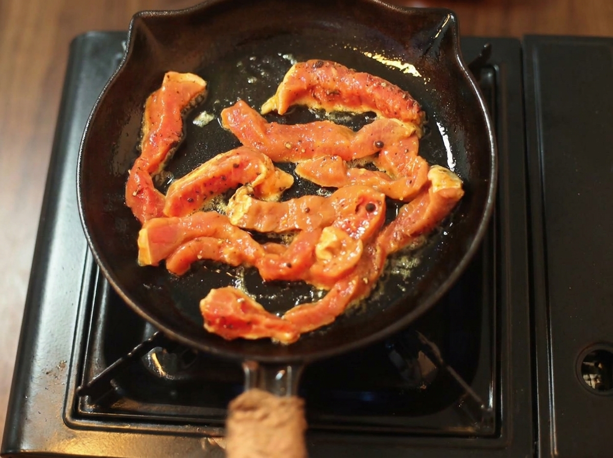 熱い黒い鋳鉄製のフライパンで、味付けされた牛肉がジューっと焼けている様子。