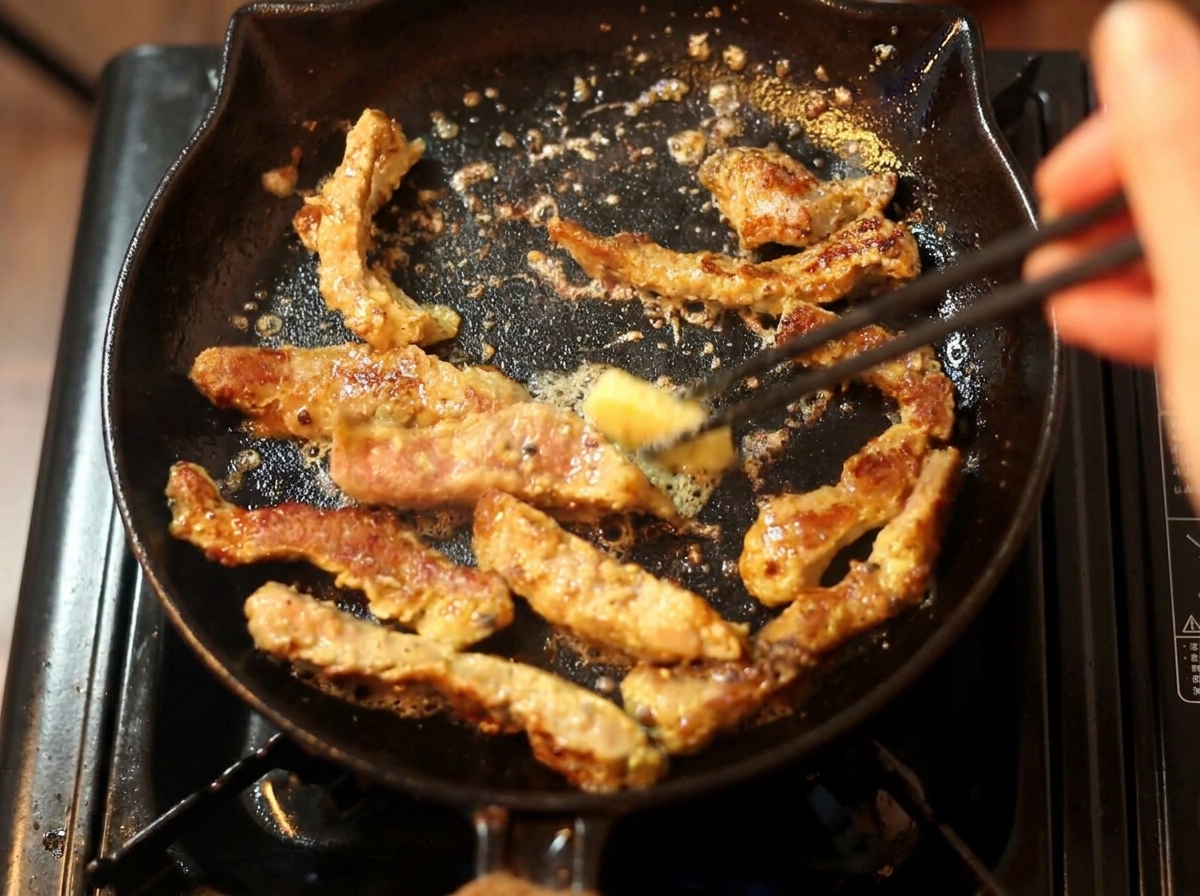 焼いている牛肉に、箸でバターをのせている様子。
