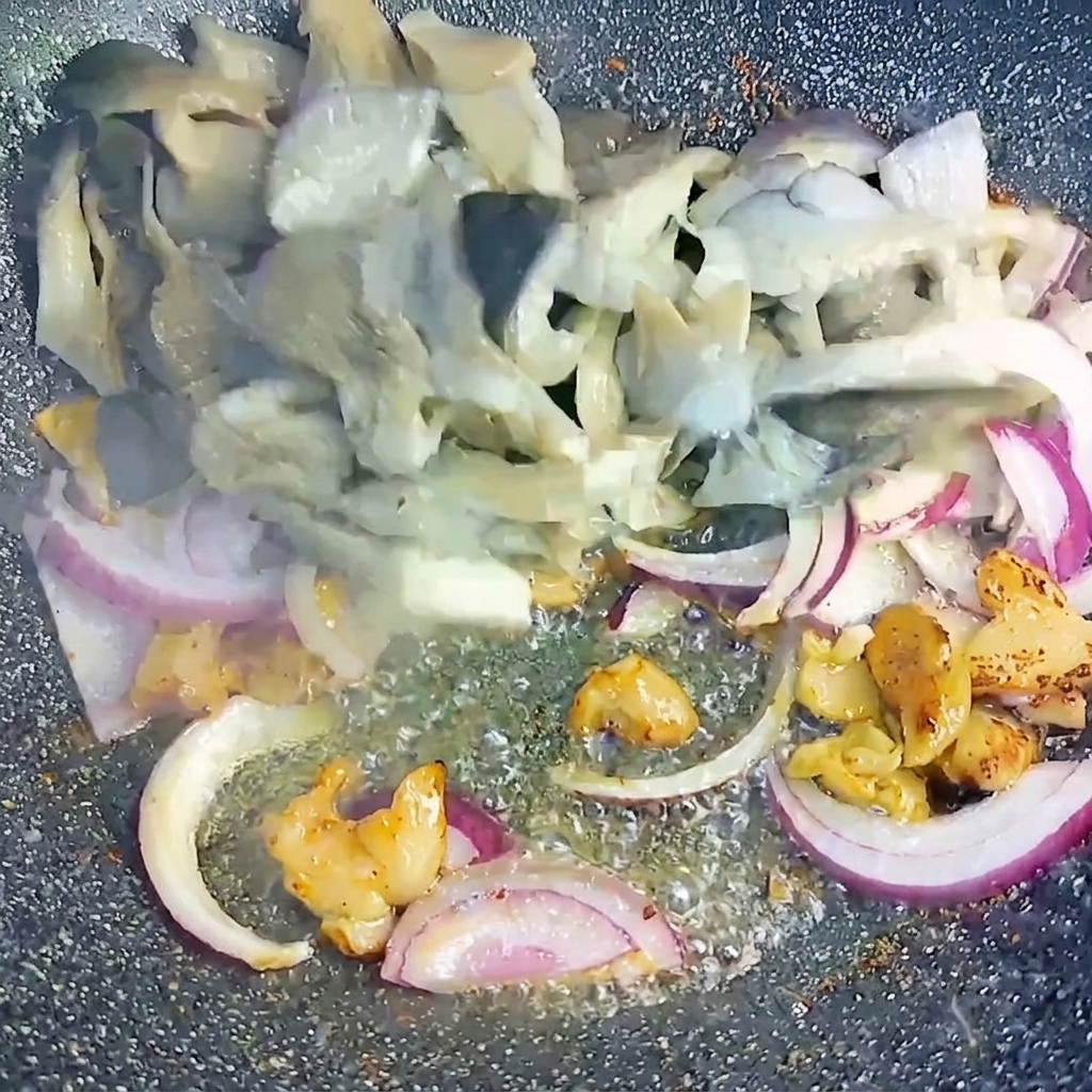中華鍋の中で、下茹でしたヒラタケとスライスした紫玉ねぎを豚バラ肉と一緒に炒め合わせている様子。