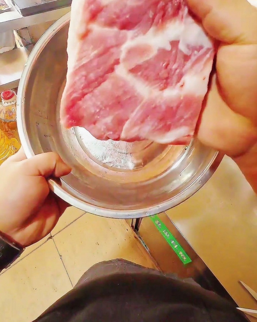 まな板の上で、生の豚バラ肉を包丁で均一な短冊状に切っている様子。