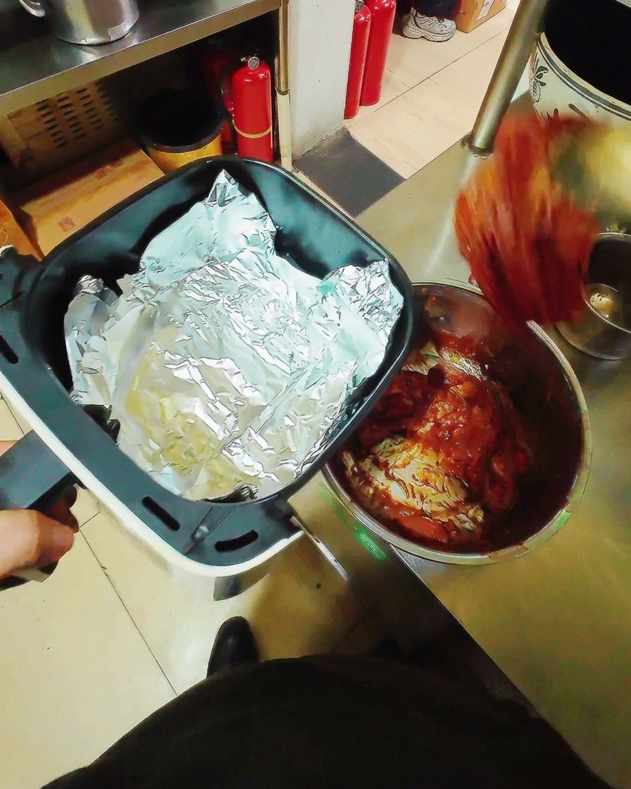 アルミホイルを敷いたエアフライヤーのバスケットに、漬け込んだ豚肉を重ならないように並べている様子。