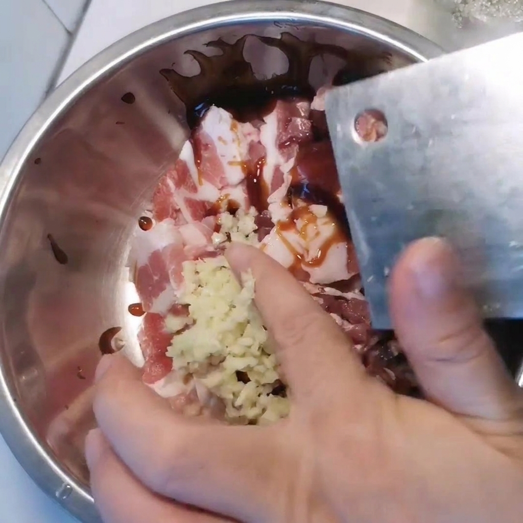 ボウルに入った豚バラ肉に、にんにくや調味料を加えている様子。