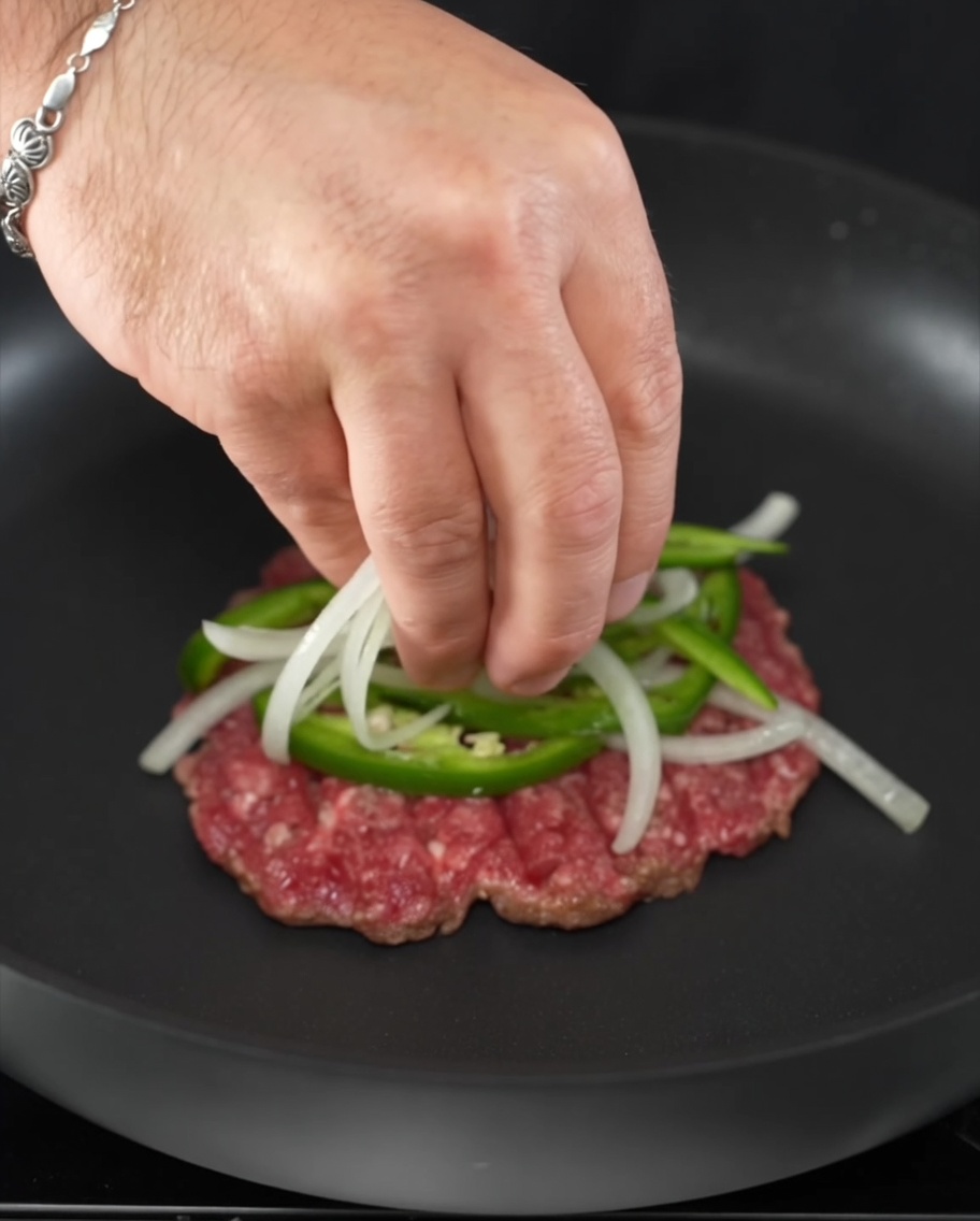 焼けているパティの上に、薄切りのハラペーニョと玉ねぎをのせている様子。