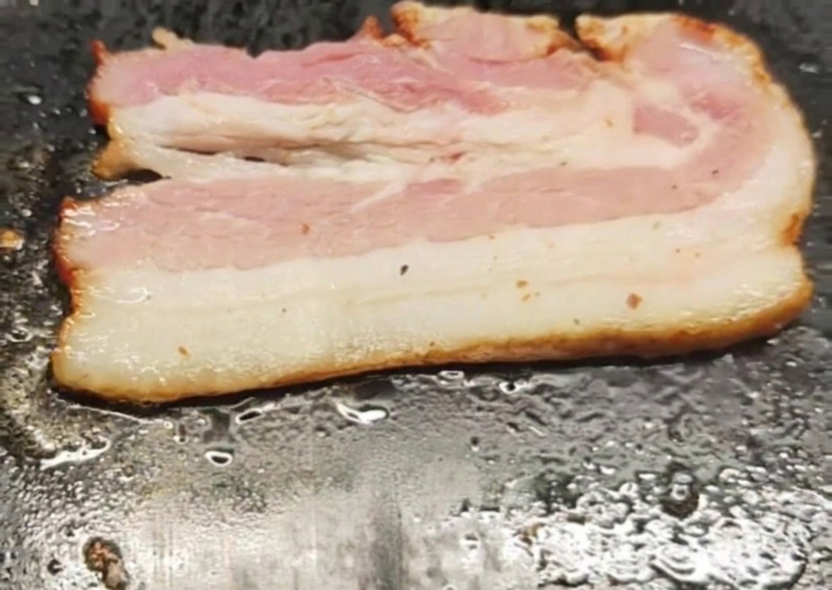 熱い鉄板の上でジューシーに焼かれている1枚のベーコン。