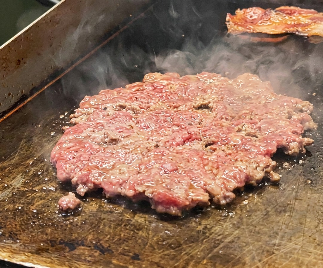 鉄板で焼かれ、塩で味付けされて玉ねぎのスライスが乗った薄いビーフパティ。