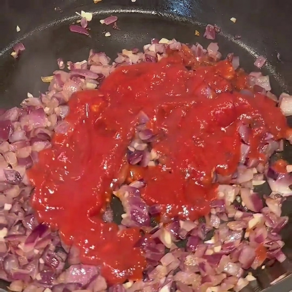 炒めた野菜が入ったフライパンにトマトピューレを注いでいる様子。