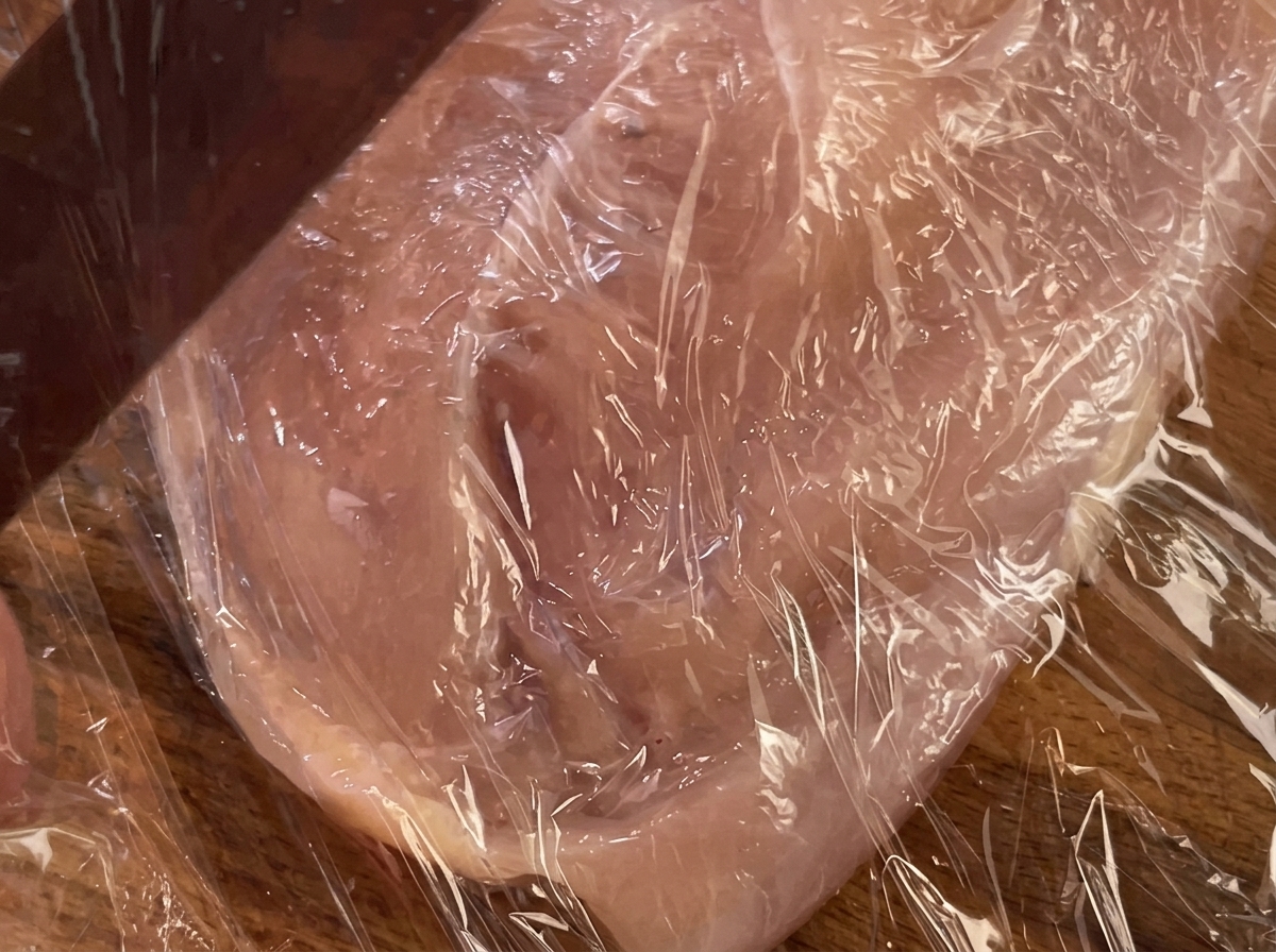 ラップに包まれた鶏胸肉を麺棒で押さえている様子。