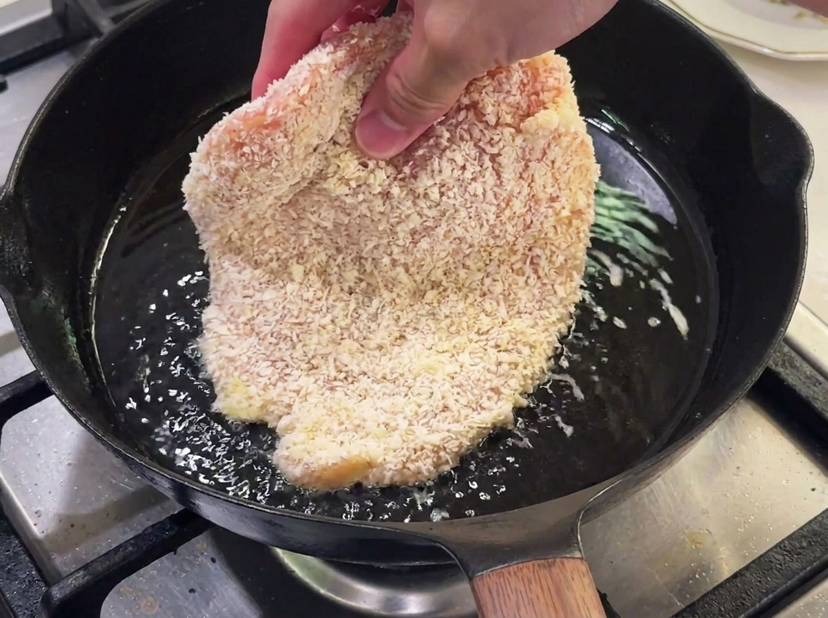 熱した油の入ったフライパンで鶏胸肉を揚げ焼きにしている様子。