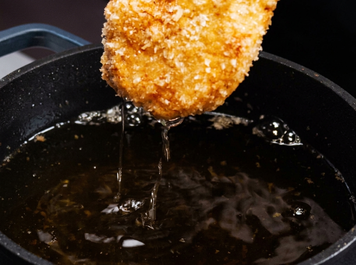 揚げ色が付いてきつね色になったチキンカツがフライパンにある様子。
