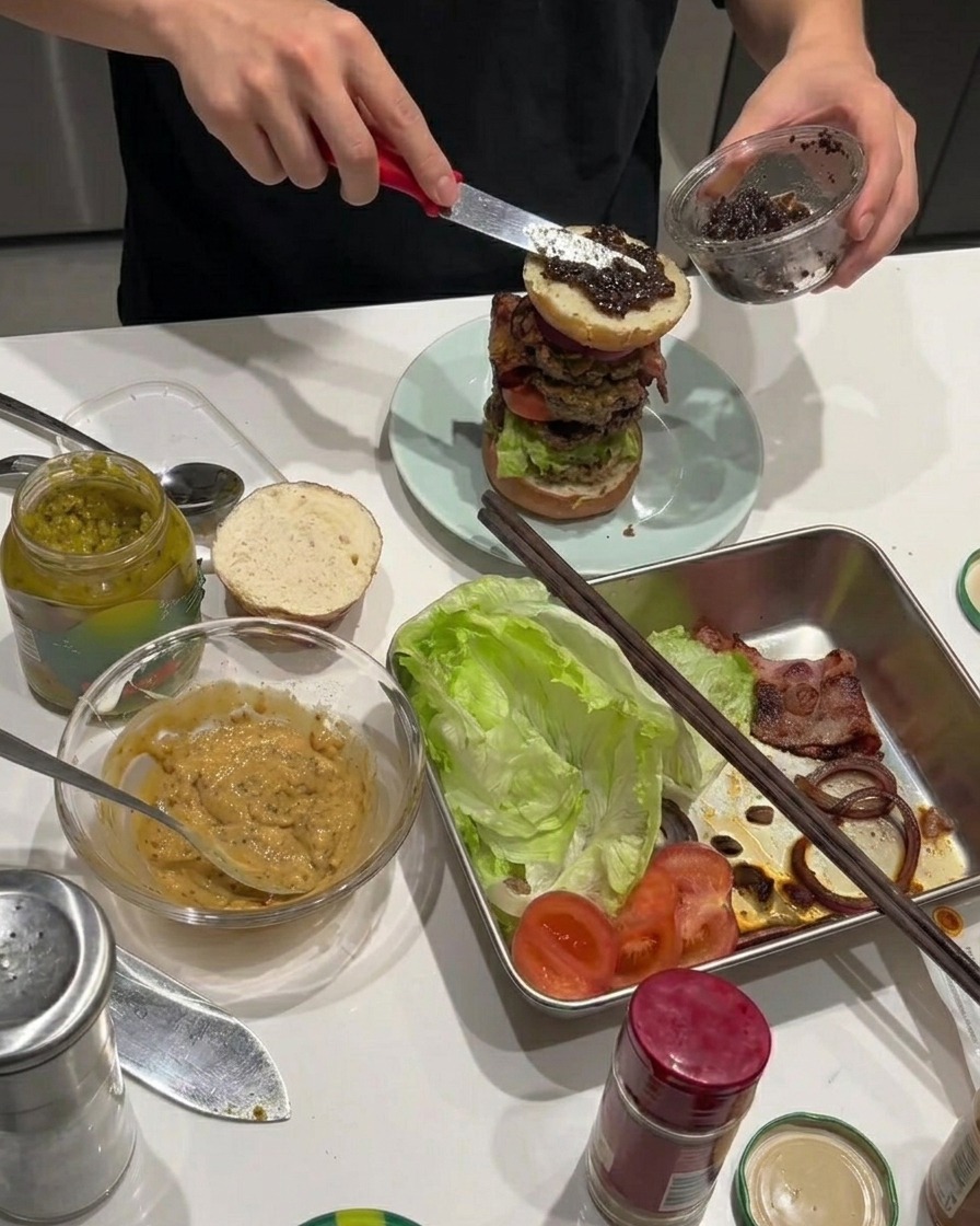 積み上げたバーガーの揚げ玉ねぎの上に黒トリュフペーストを塗っている様子。