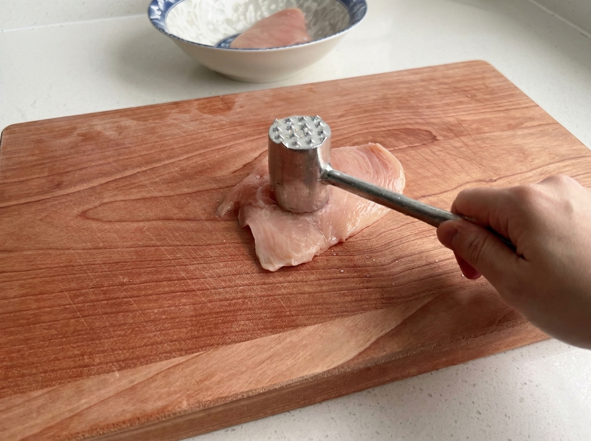 まな板の上で肉叩きを使って鶏むね肉を叩いている様子。