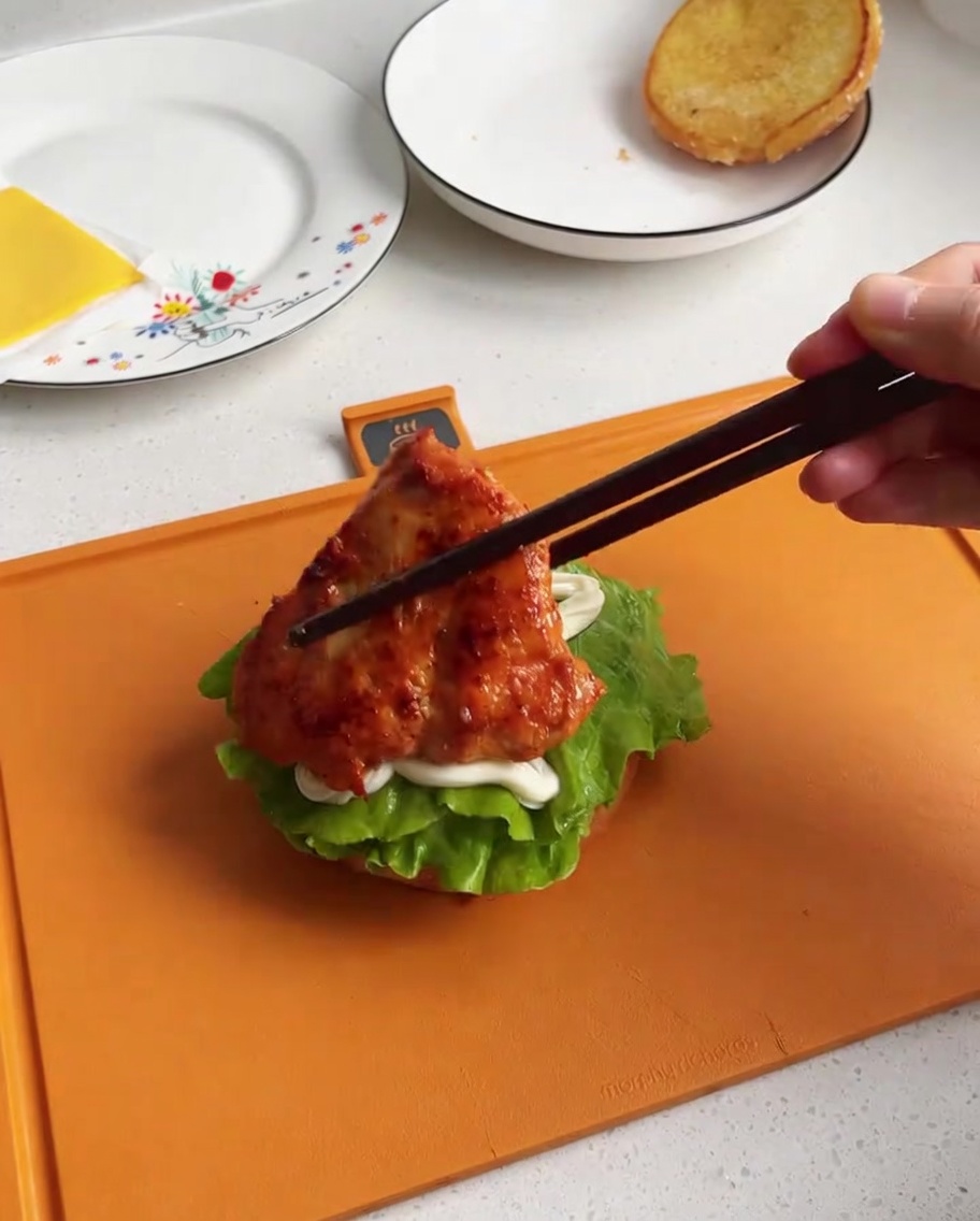 マリネされ焼かれたチキンをバンズ上のレタスの上に載せている様子。