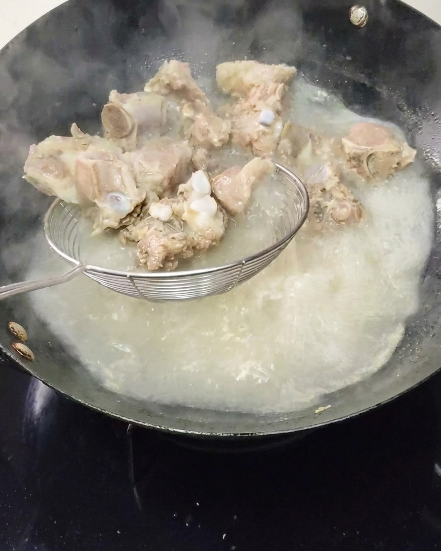 アク取り網を使って、沸騰した鍋からリブを引き上げている様子。