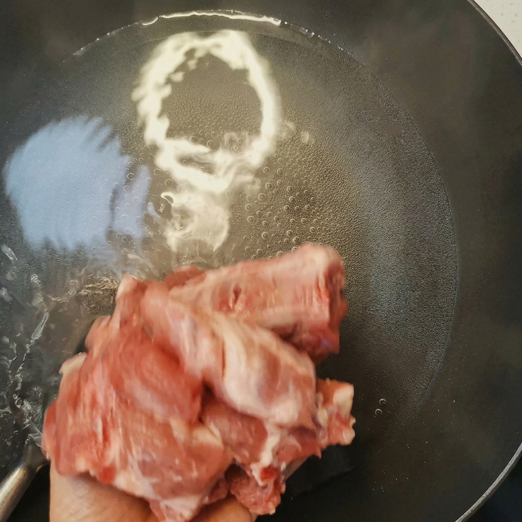鍋で料理酒と共に下茹でされ、表面にアクが出てきた豚スペアリブ。