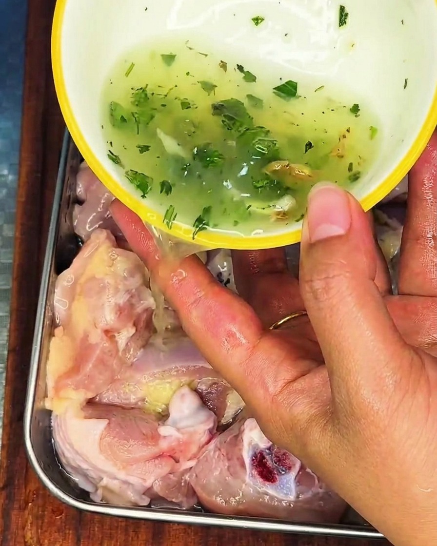 ネギと生姜の香りを移した液体を、ステンレス容器の生の鶏肉にかけている様子。