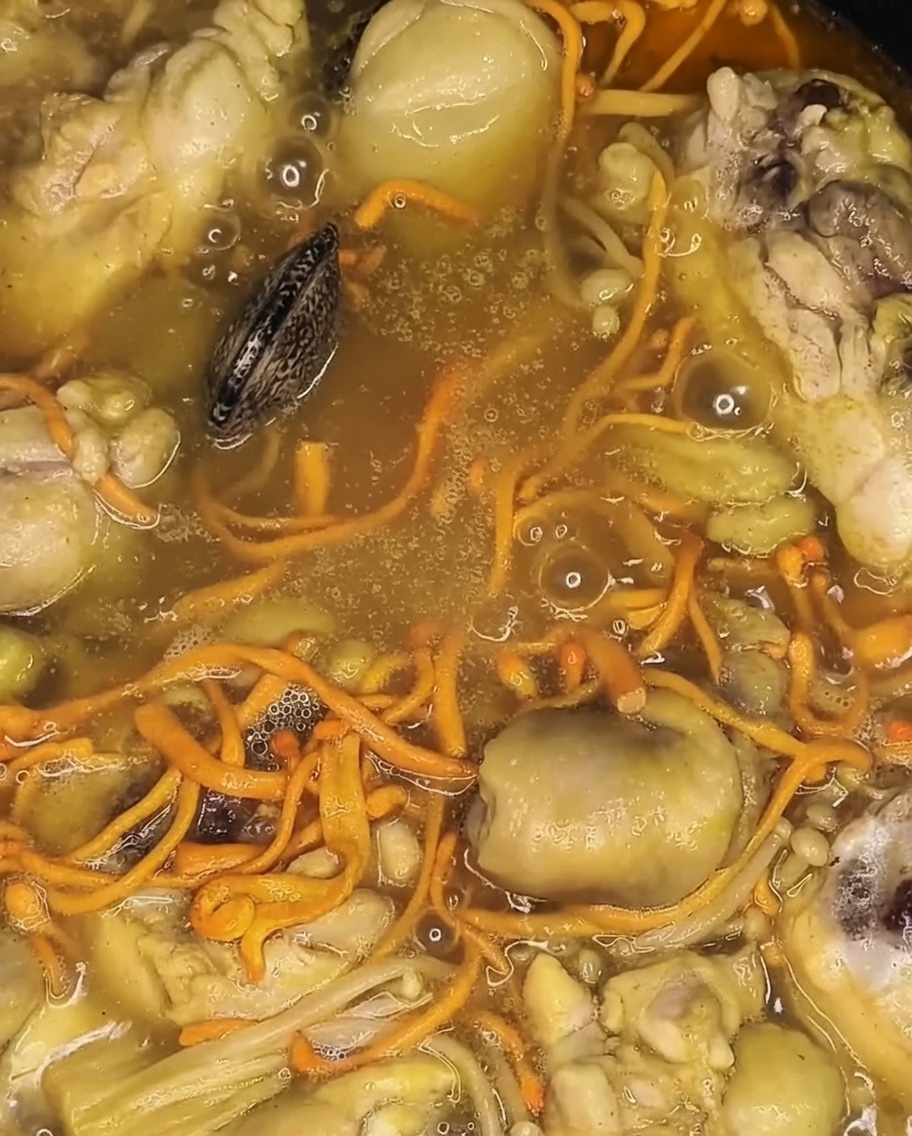 煮込んでいる鶏肉や野菜の上に、新鮮なアサリを加えている様子。