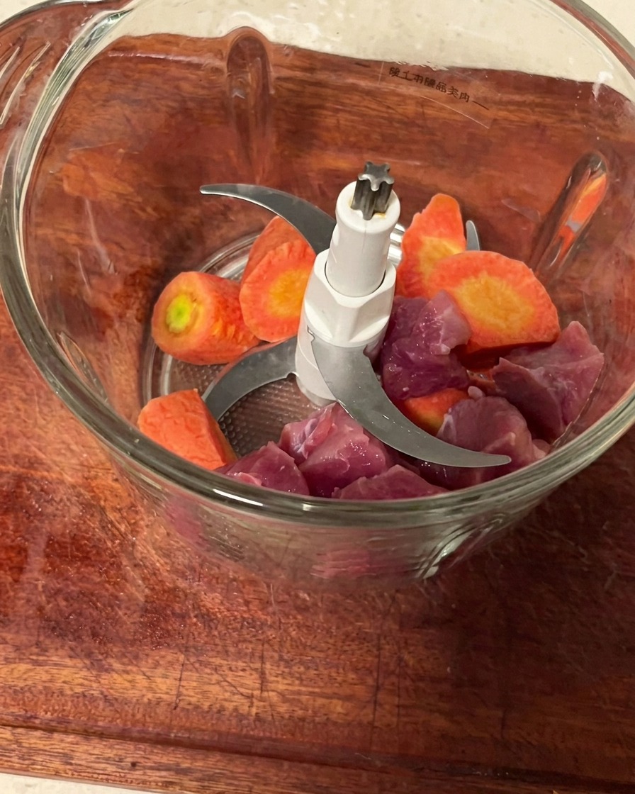 ミンサーの容器に入れられた、一口大に切った豚肉と人参。