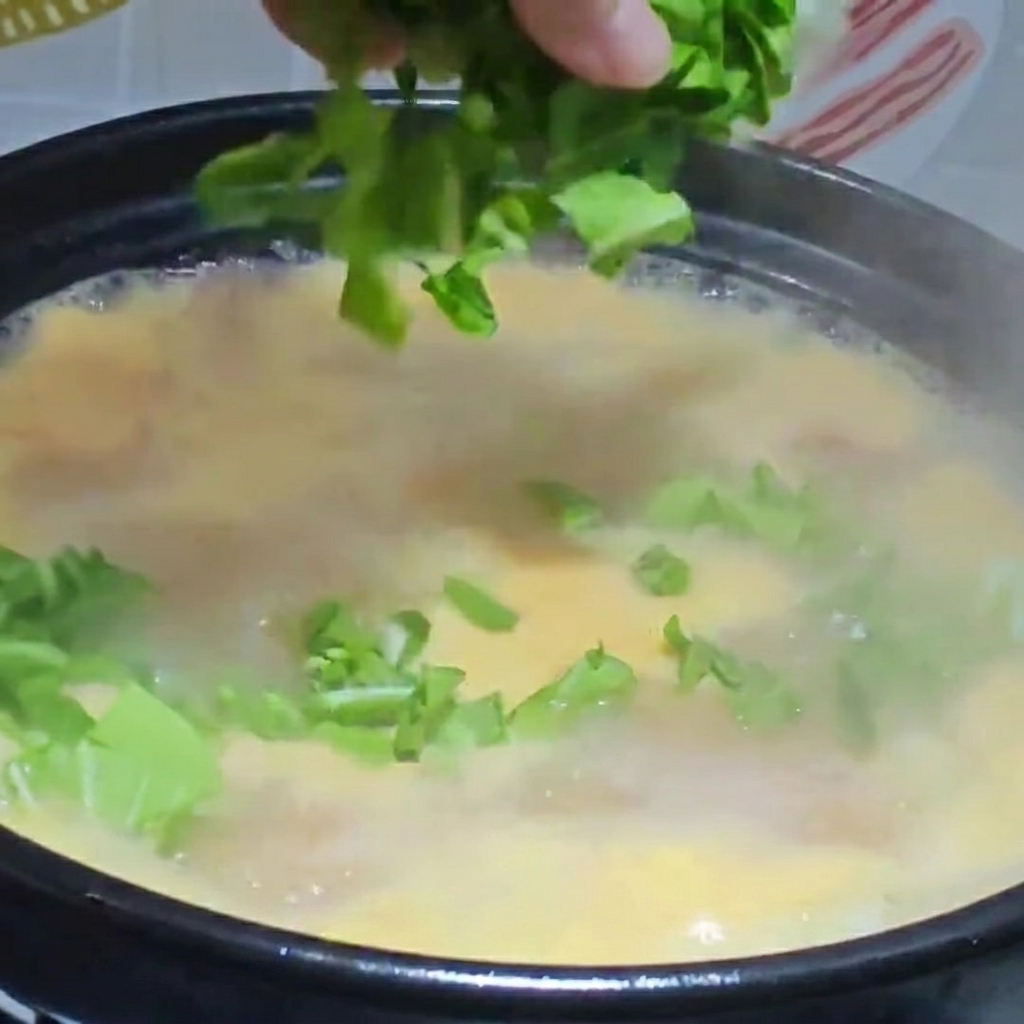 刻んだ葉物野菜とほぐした鶏肉を、完成間近のすいとん入りスープ鍋に入れている様子。