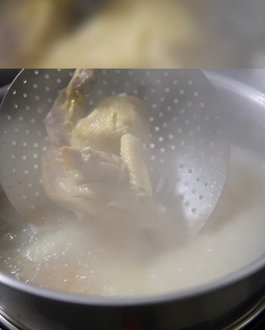 煮立っているスープの中に、蒸し上がった丸鶏を静かに沈めている様子。