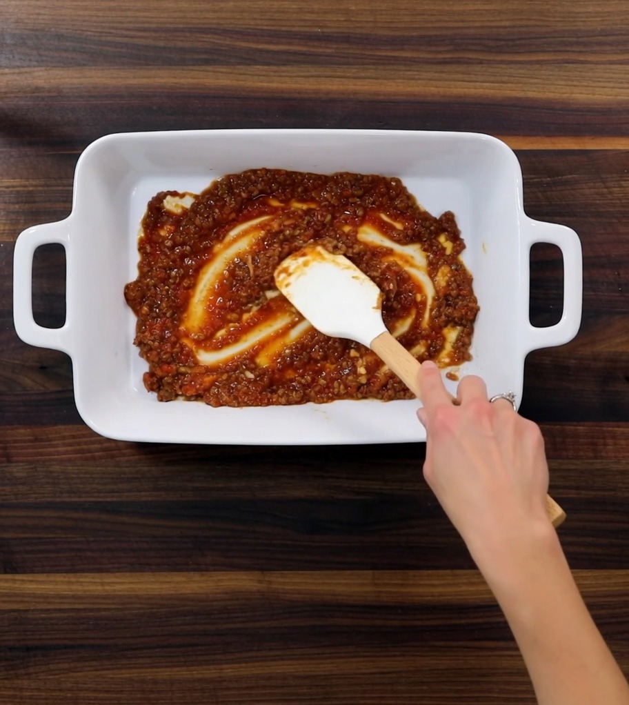 耐熱皿の中に、ミートソース、パスタ、ホワイトソースの層が交互に重ねられている様子。
