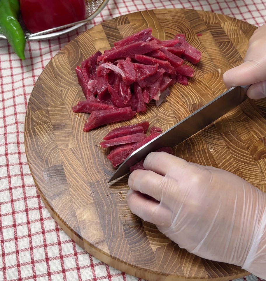 まな板の上で生の牛肉を薄切りにしている様子。
