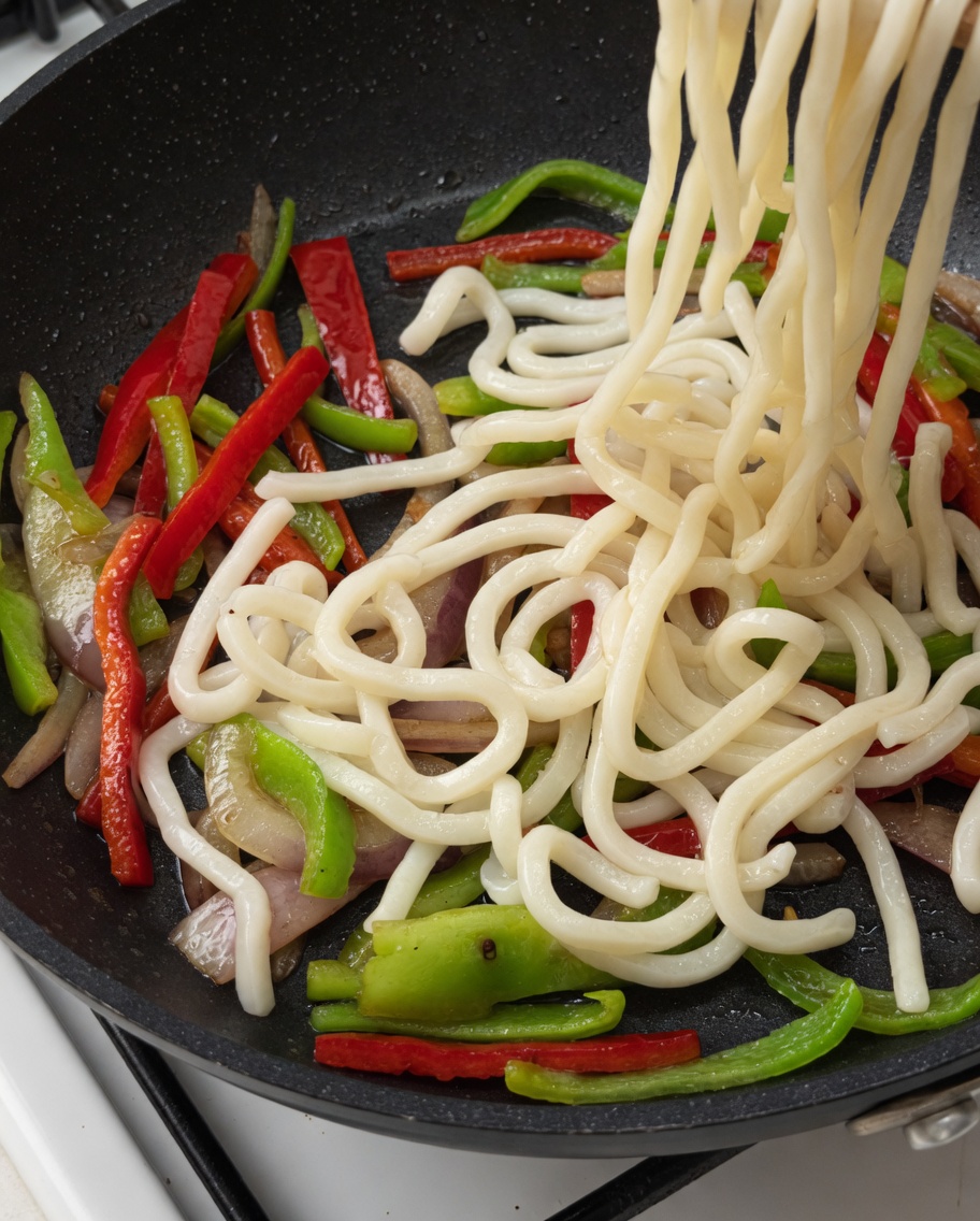 具材の入ったフライパンにうどんと肉を加える様子