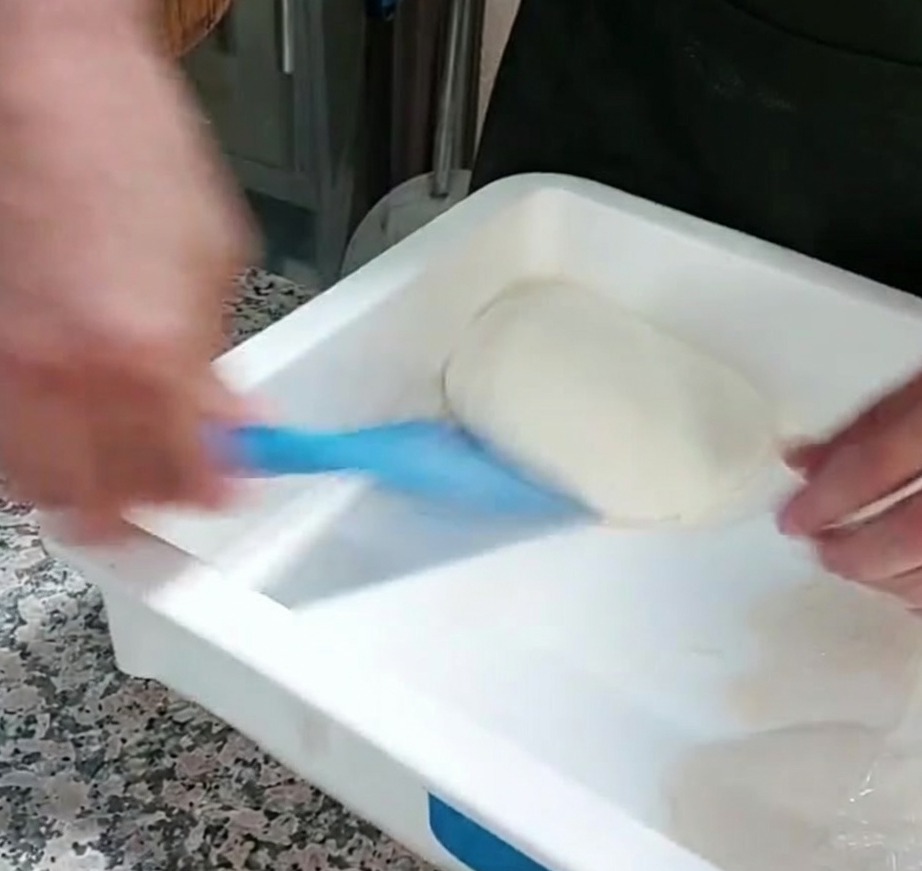 プラスチック製のドゥスクレーパーを使って容器からピザ生地を取り出す様子。