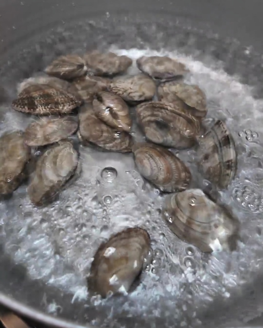 ぐつぐつと沸騰した鍋の中で茹でられている新鮮なアサリ。