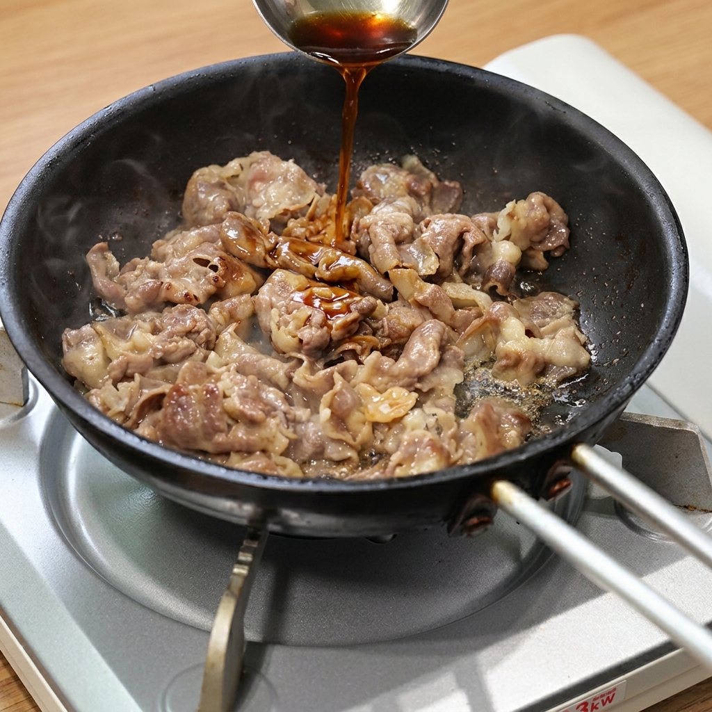 こんがり焼けた薄切り牛肉に、金属製のおたまですき焼きのタレをかけている様子。