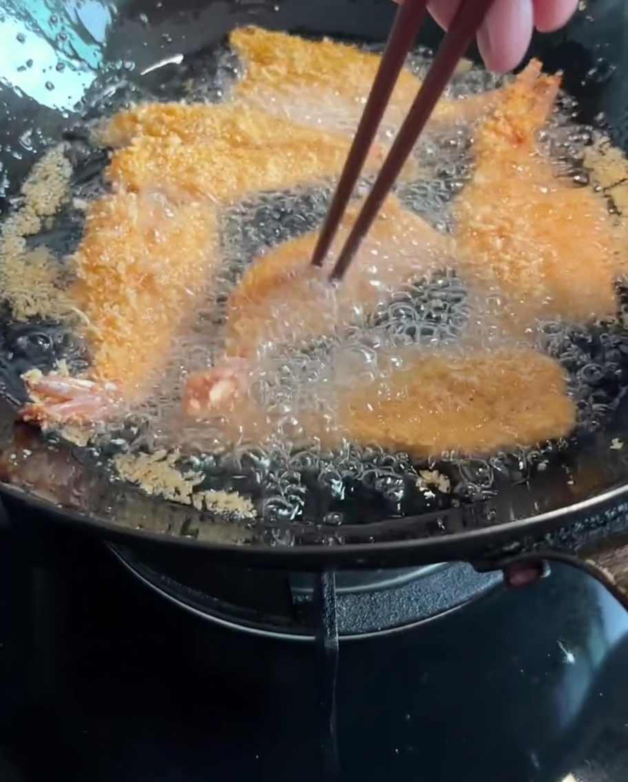菜箸で油の中の海老を裏返している様子。